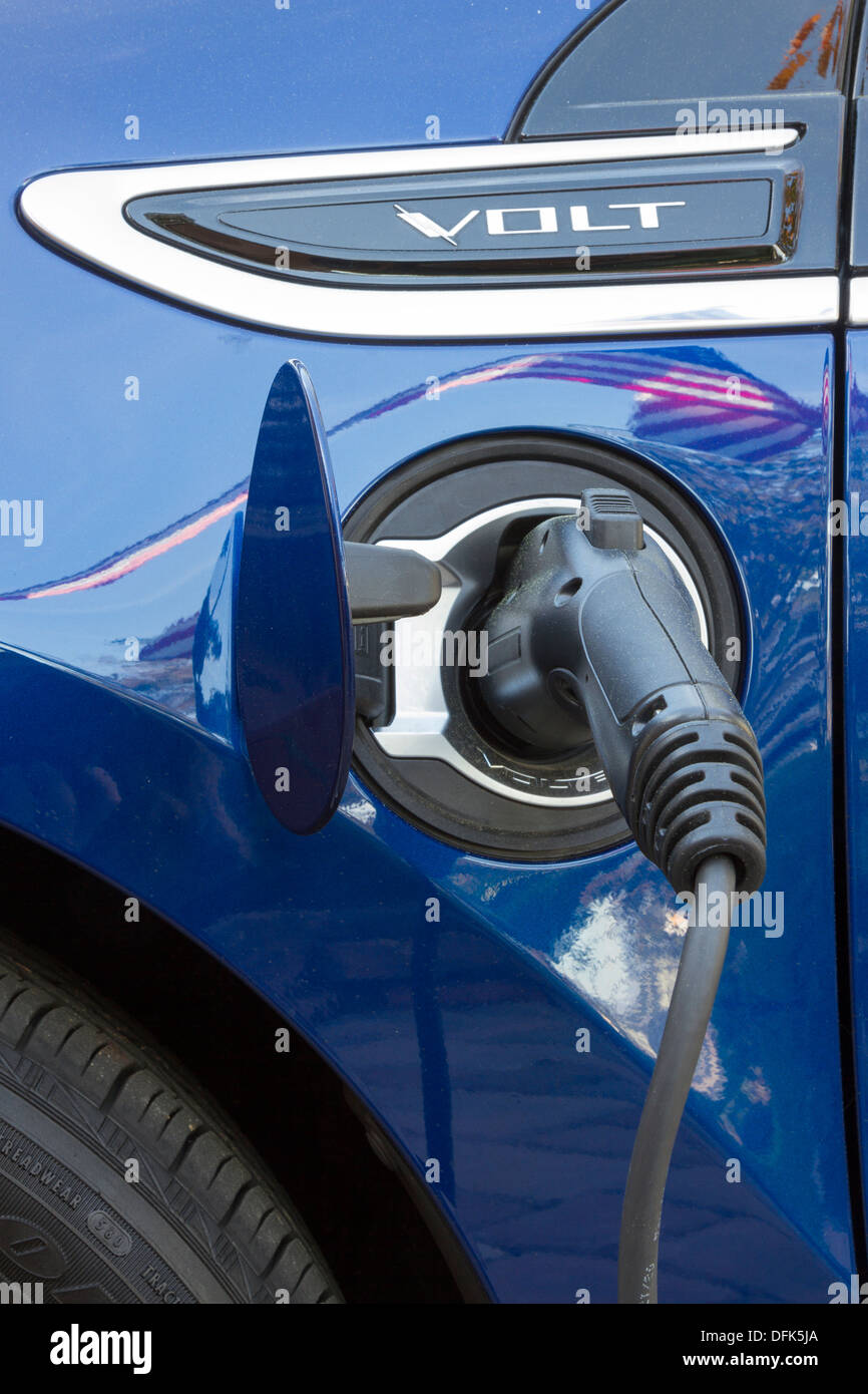 Chevrolet Volt plug-in electric vehicle with connector plugged in and charging with reflection of American flag on car Stock Photo
