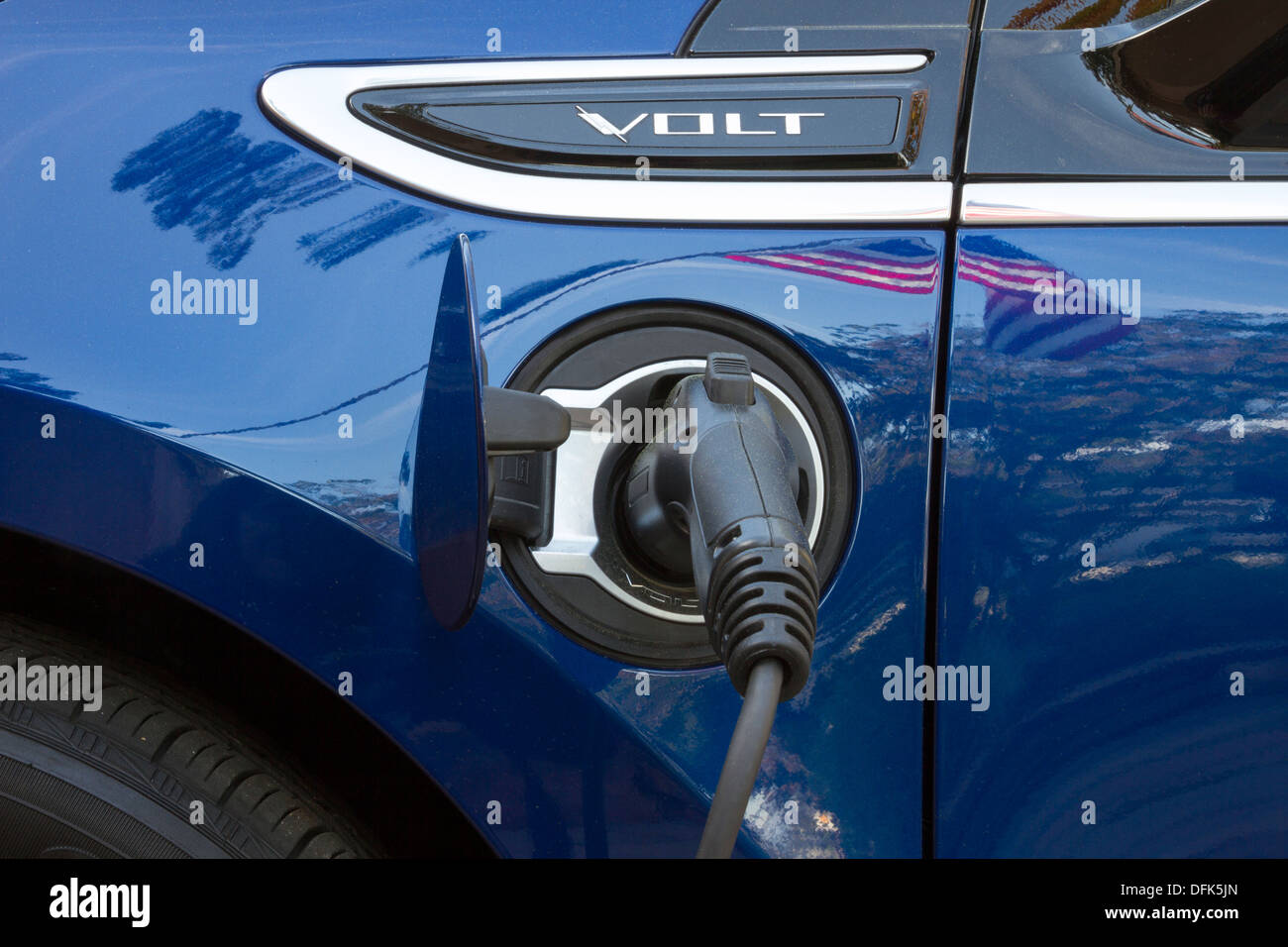 Chevrolet Volt plug-in electric car with connector plugged in and charging with reflection of American flag on vehicle Stock Photo