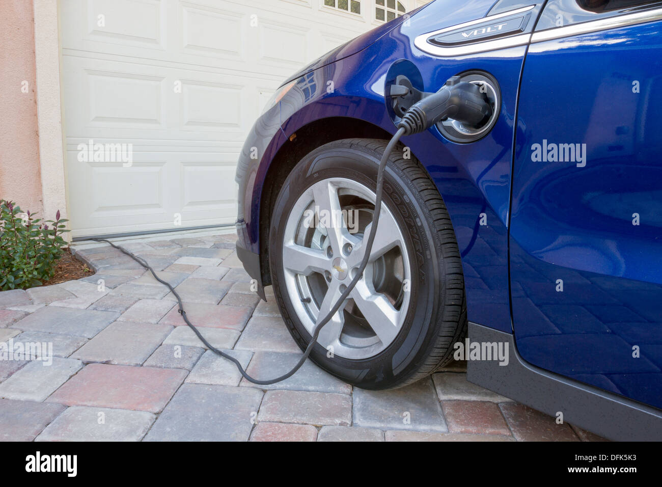 Chevrolet Volt plug-in electric car with connector plugged in charging, at home in a driveway Stock Photo