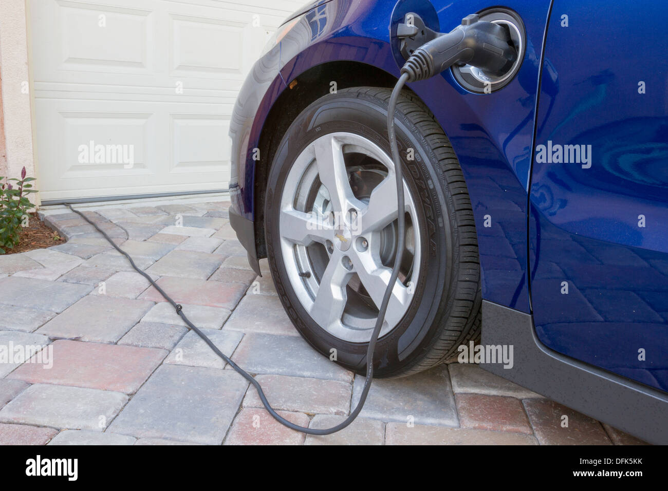 Plug-in hybrid electric car with connector plugged in and charging at home in a driveway Stock Photo