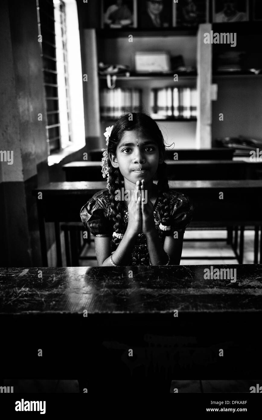 Indian girl sitting at a school desk with prayer hands. Andhra Pradesh, India. Black and White. Stock Photo