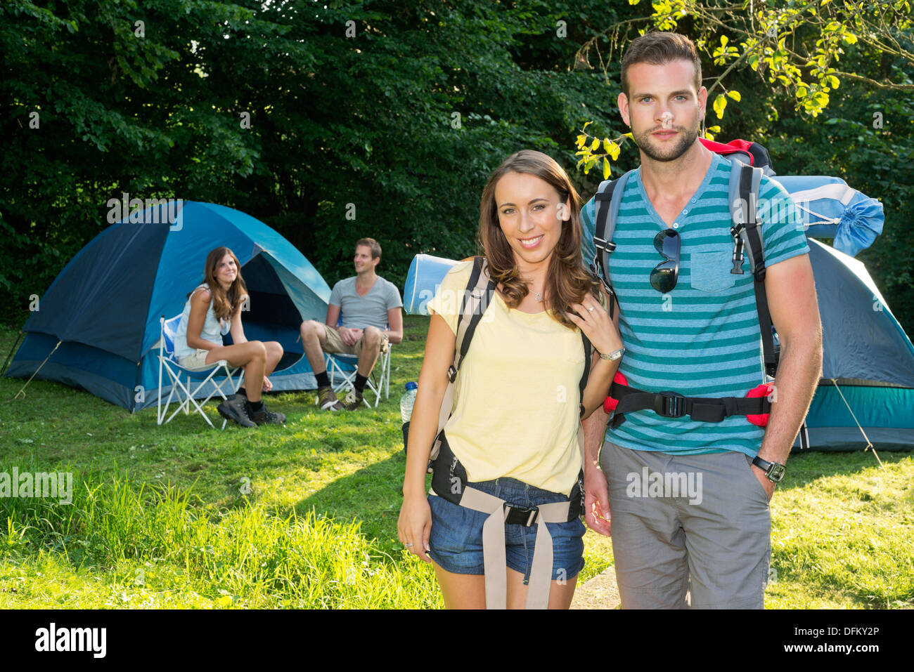 Portrait of a young couple standing in front of tents, friends in the background Stock Photo