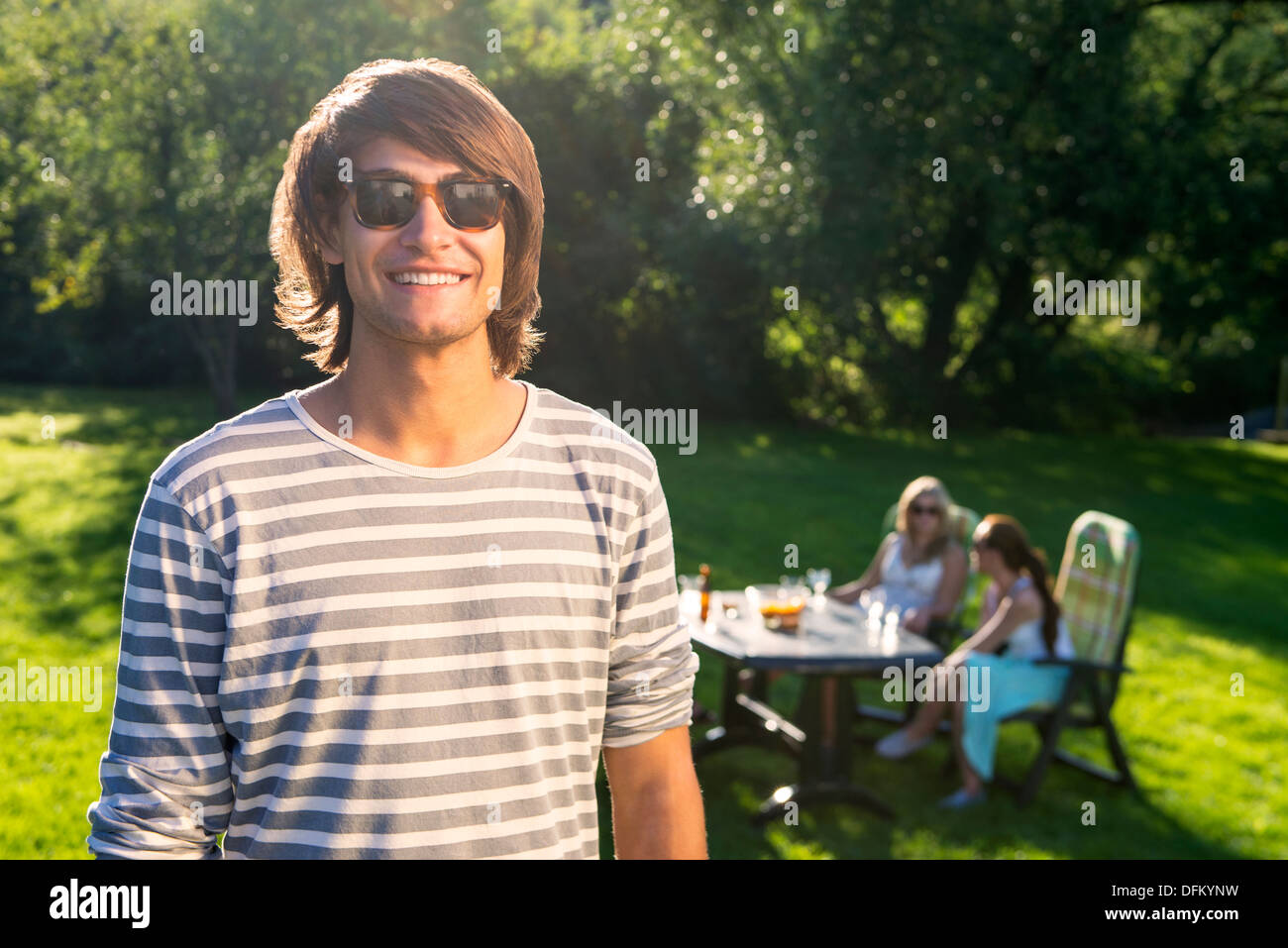 A young man standing in a sunny garden while his friends enjoying a garden party in background Stock Photo