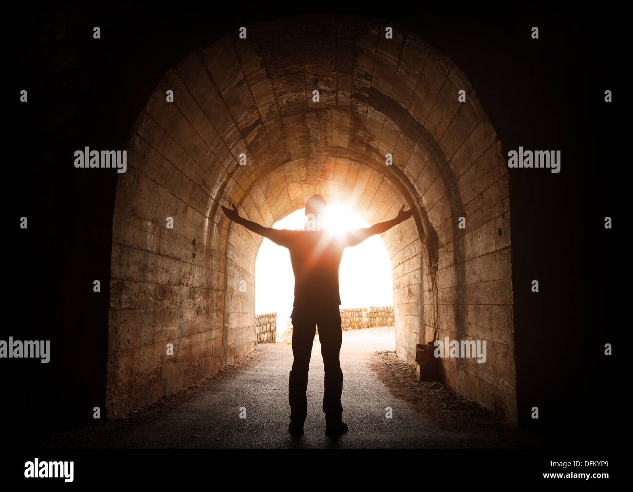 Man stands inside of old dark tunnel with shining sun in the end Stock Photo
