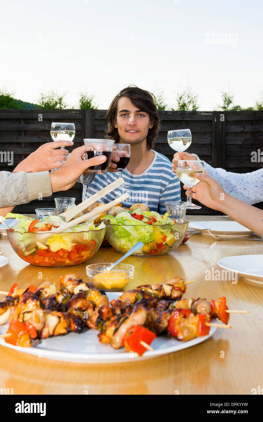 Portrait of young man toasting drinks with friends at table during outdoor party Stock Photo