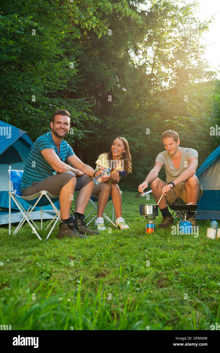 Three friends cooking in front of tents Stock Photo