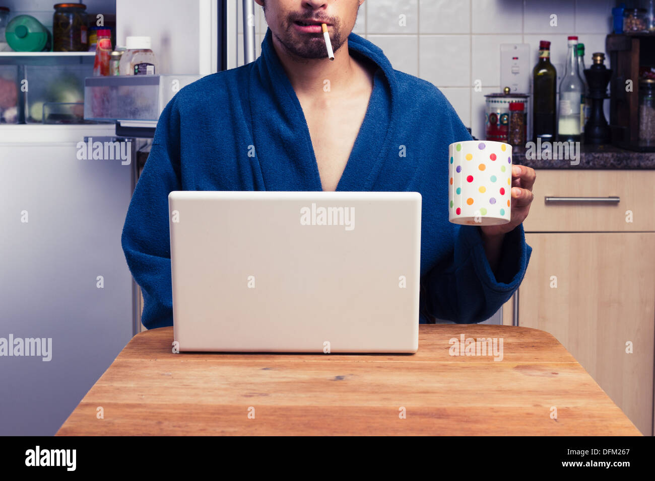 Young man in bathrobe smoking and using laptop Stock Photo