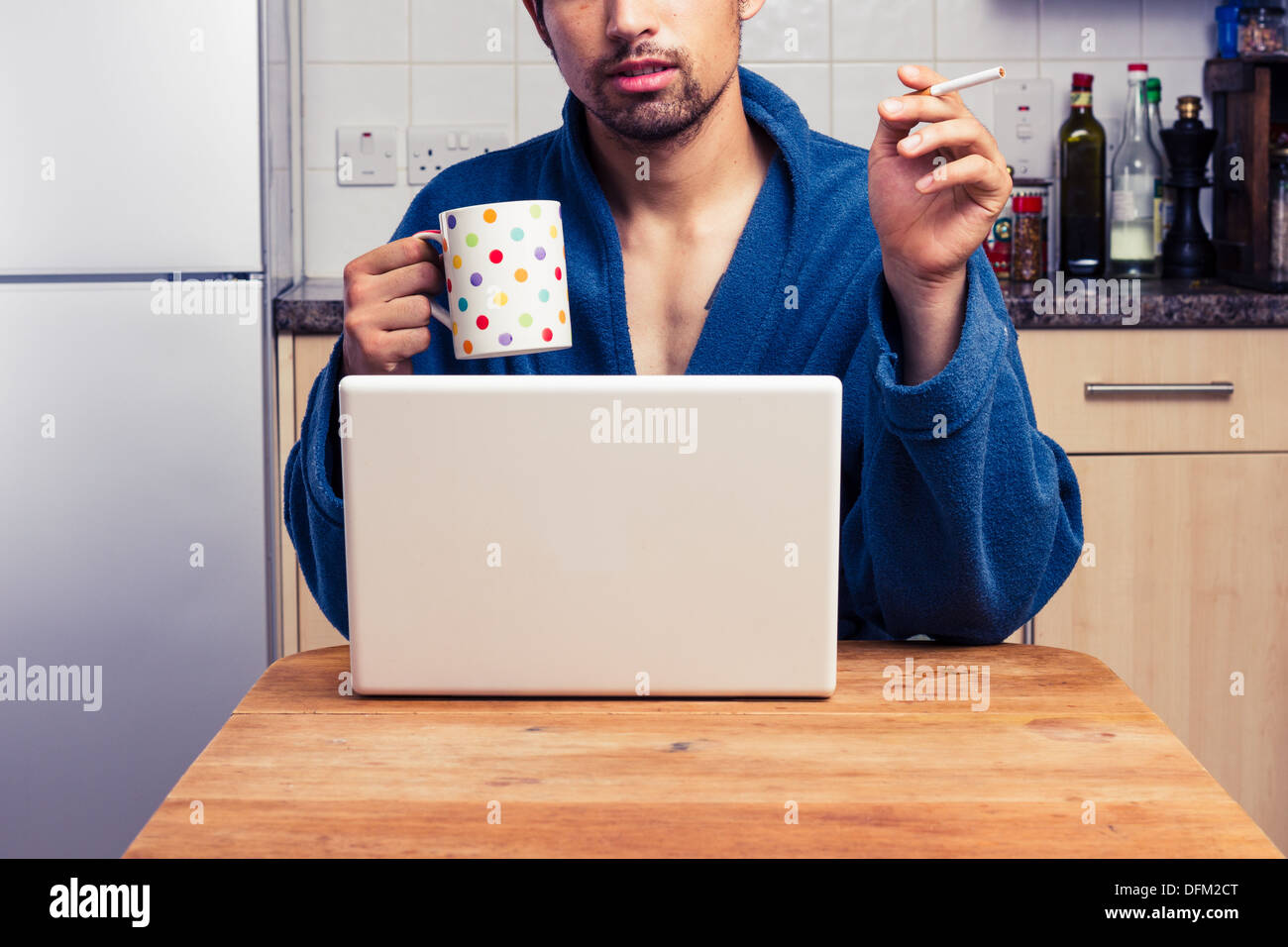 Young man in bathrobe using laptop and smoking Stock Photo