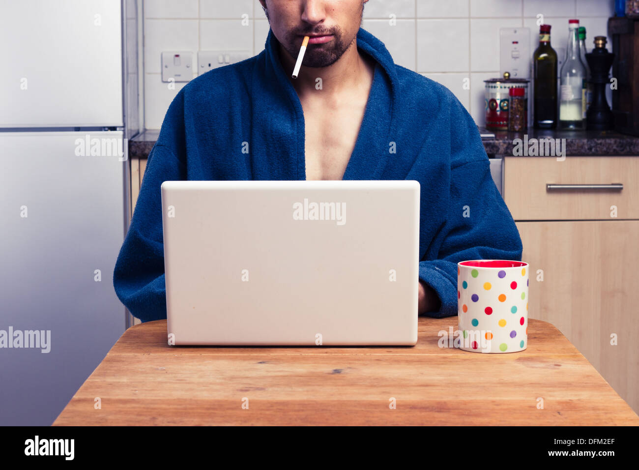 Young man in bathrobe using laptop and smoking Stock Photo