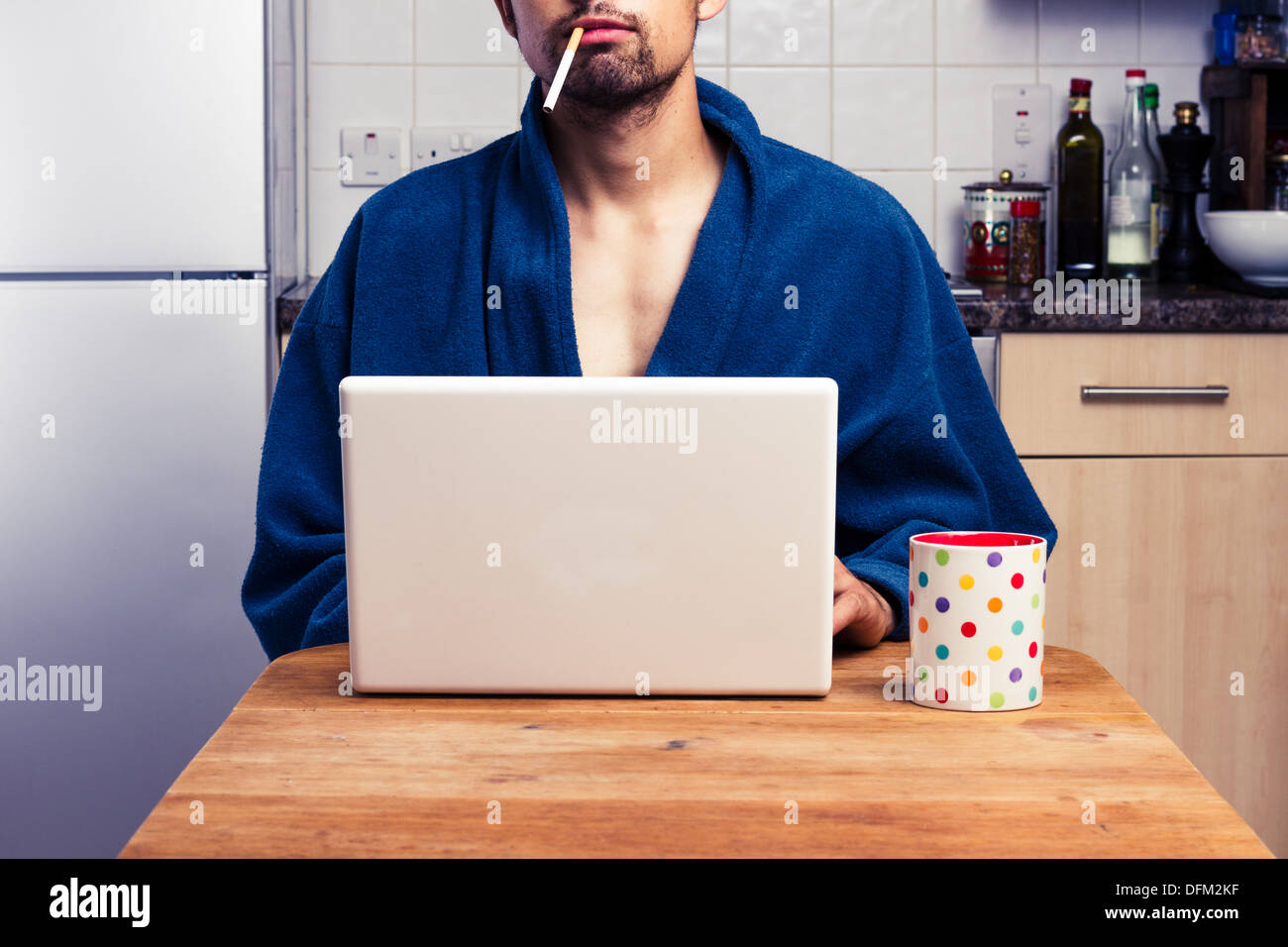 Young man using laptop and smoking in kitchen Stock Photo