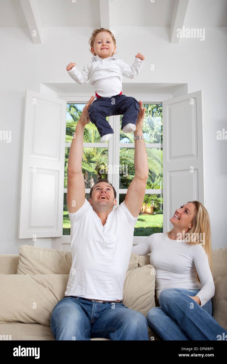 Family on their sofa throwing one year old baby in the air Stock Photo
