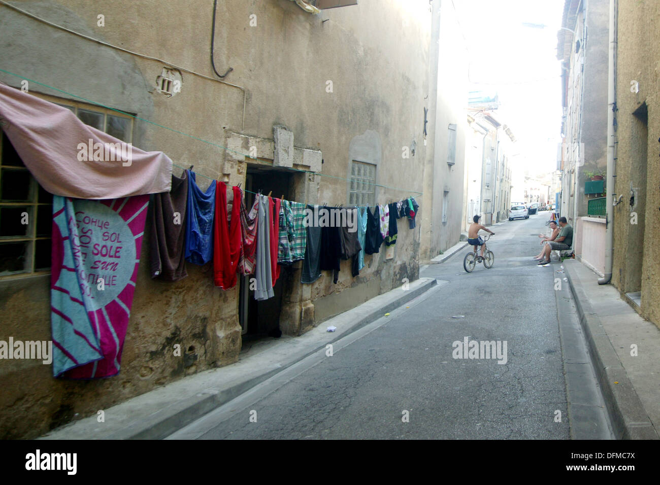 street scene in small french town with washing hanging by the side of the road whilst people rest on the pavement Stock Photo
