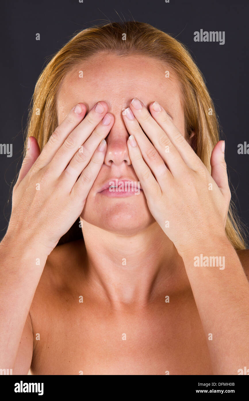 A young woman covering her eyes with her hands The three wise monkeys.  See no evil, see no evil, speak no evil Stock Photo