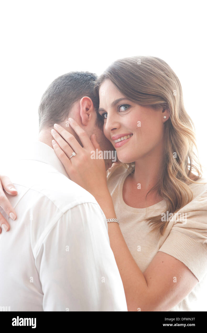High key image of a late 20s/early 30s male and female couple embracing and in love. Woman giving a knowing and thoughtful look. Stock Photo