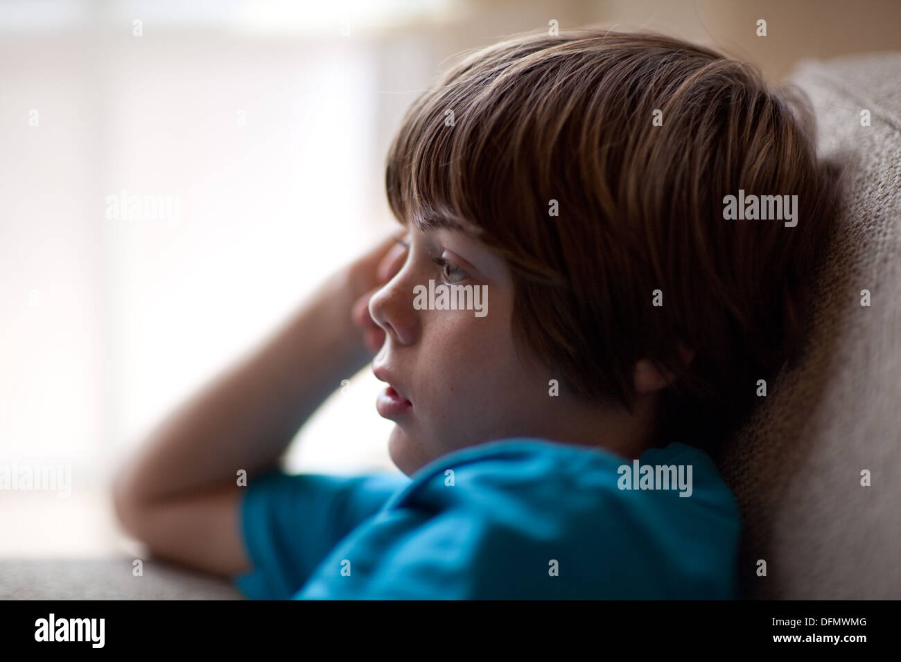 Profile of ten year old boy watching tv with blank, tired expression. Stock Photo