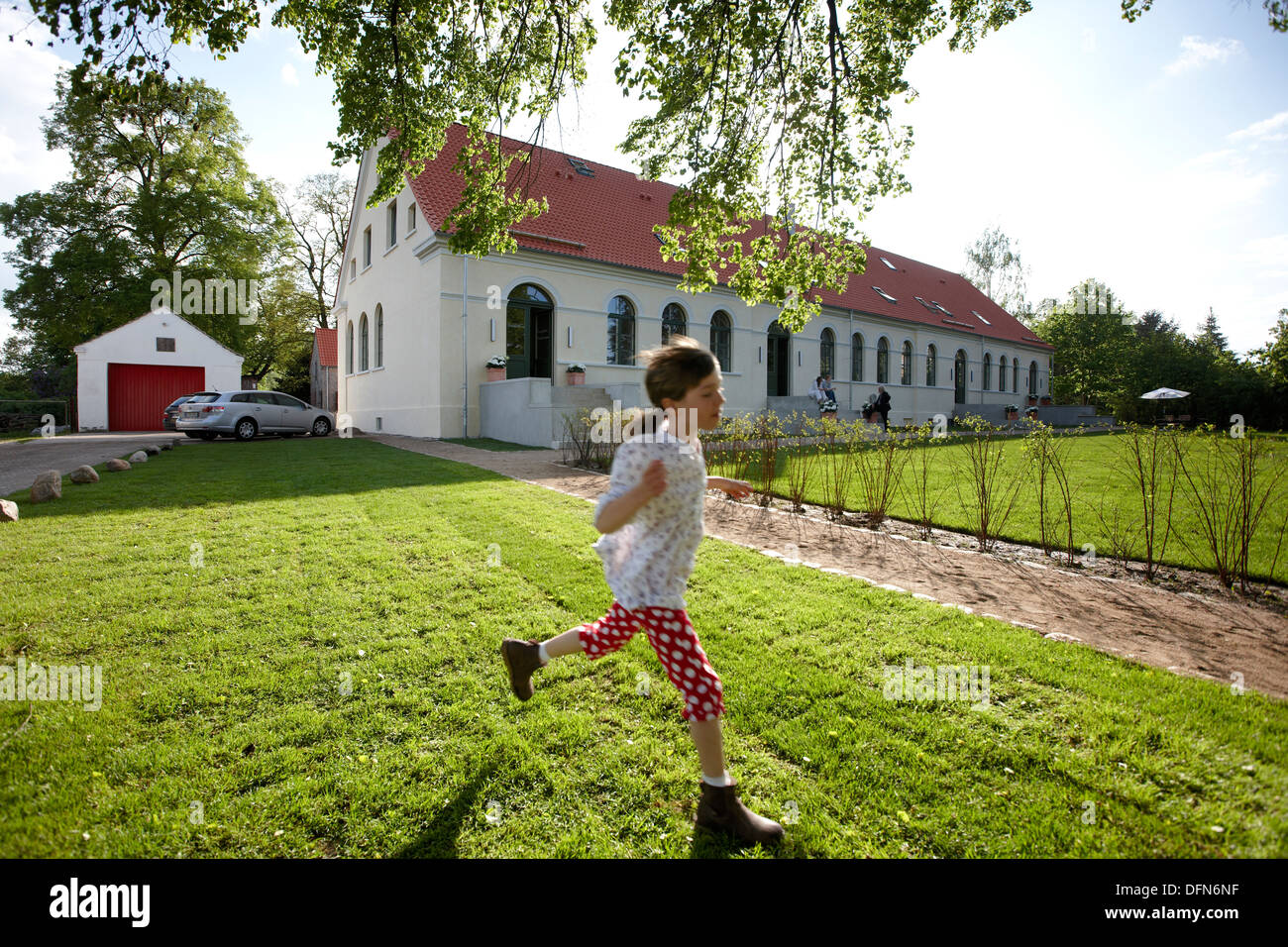 Girl running over a meadow near an hotel, Fincken, Mecklenburg-Western Pomerania, Germany Stock Photo