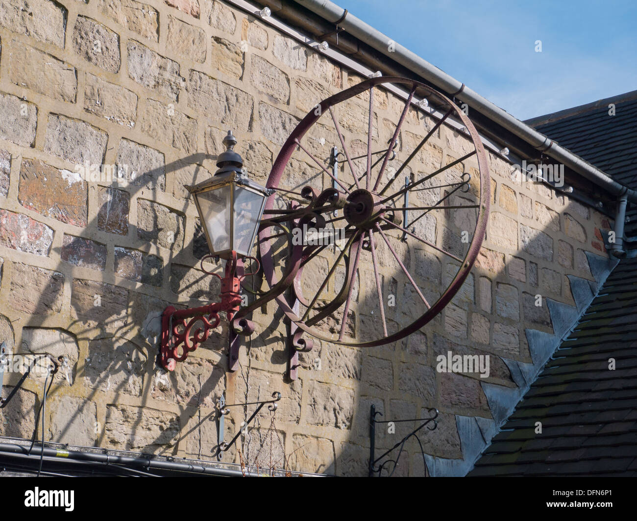 Old rusty wheel on the wall out side a pub in Holbrook near Belper, Derbyshire, United Kingdom, UK Stock Photo