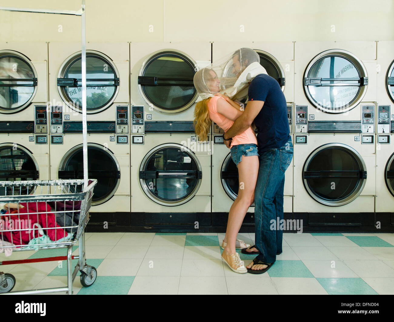A pretty woman hugs by a smart young man in San Diego coin laundromat. Stock Photo