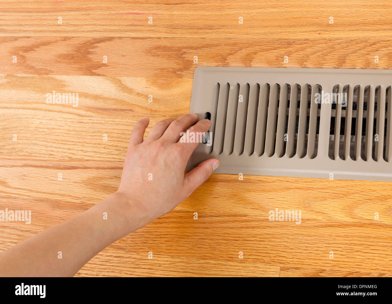 Horizontal photo of female hand opening up heater floor vent with Red Oak Floors in background Stock Photo