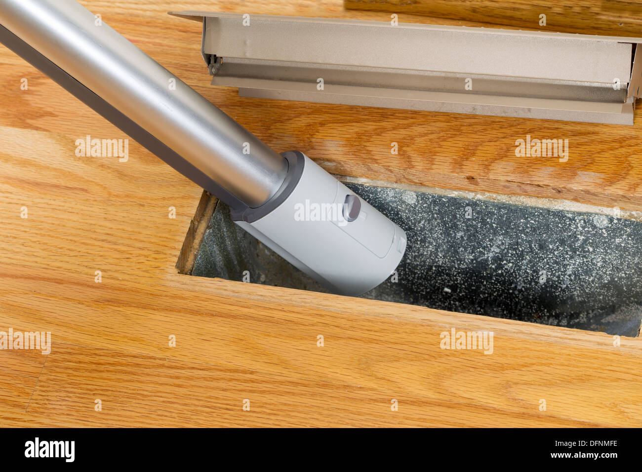 Horizontal photo of vacuum cleaning inside heater floor vent with Red Oak Floors in background Stock Photo