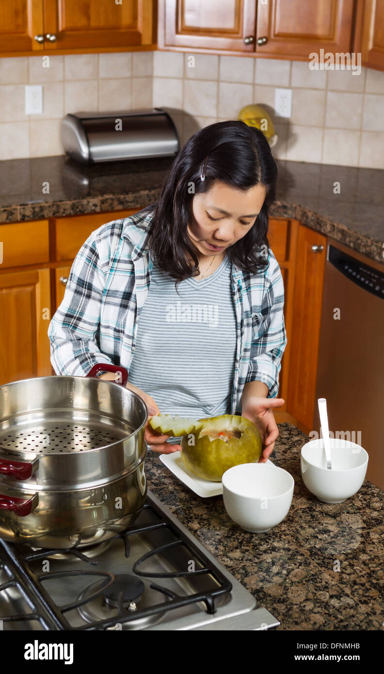 Vertical photo of mature woman putting top of cooked winter melon back on while placed in dinner plate next to cooking kettle on Stock Photo