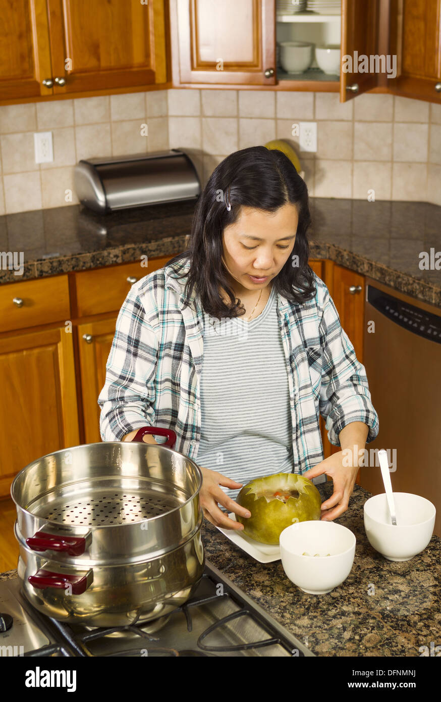 Vertical photo of mature woman working with cooked winter melon on dinner plate next to cooking kettle on stove top Stock Photo