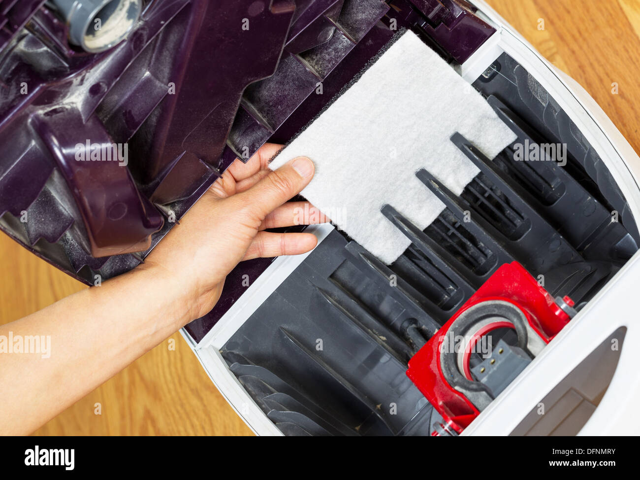 Horizontal photo of female hand installing clean vacuum cleaner filter with hardwood floors in background Stock Photo