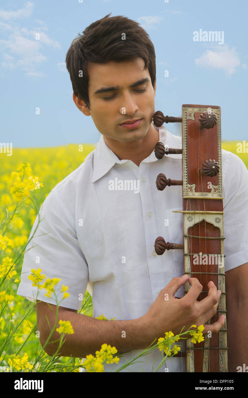 Close-up of a man playing sitar in a mustard field Stock Photo