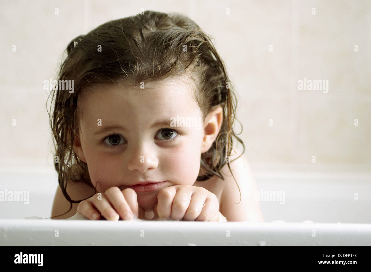 3 year old girl leaning onto the edge of the bath ,with a coy little ...