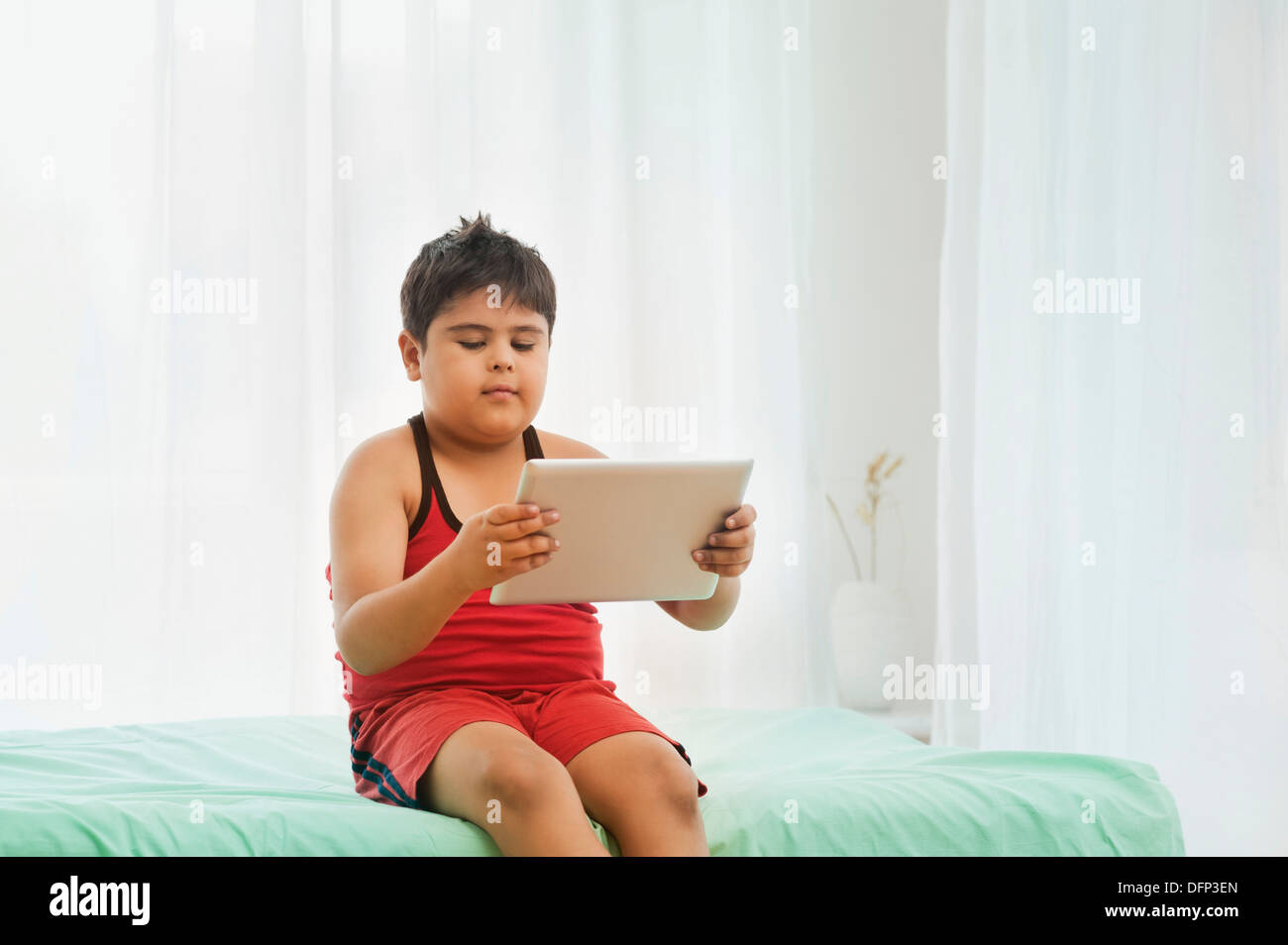 Boy sitting on the bed and using a digital tablet Stock Photo