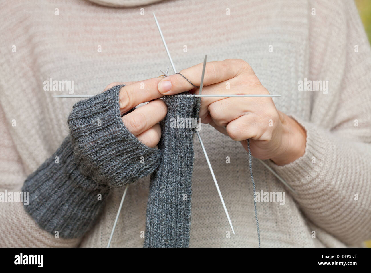 knitting emergency - female hands knitting one fingerless mitt while wearing the ready one, five-needles method Stock Photo