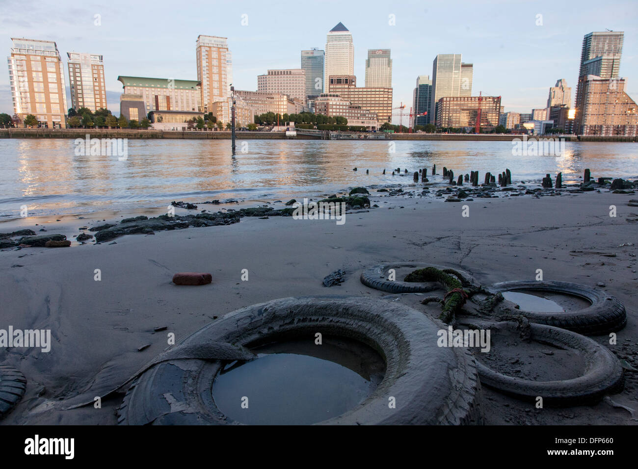 landscape view of canary wharf in daylight from opposite bank of the river thames with discarded rubber tyres buried in sand Stock Photo