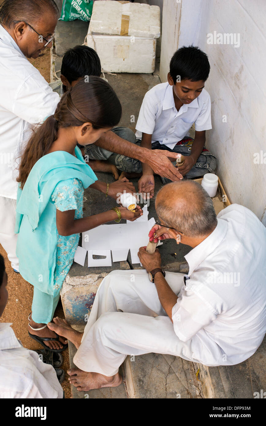 Indian man and children putting vitamin B tablets into packets at Sri Sathya Sai Baba mobile outreach hospital pharmacy. India Stock Photo