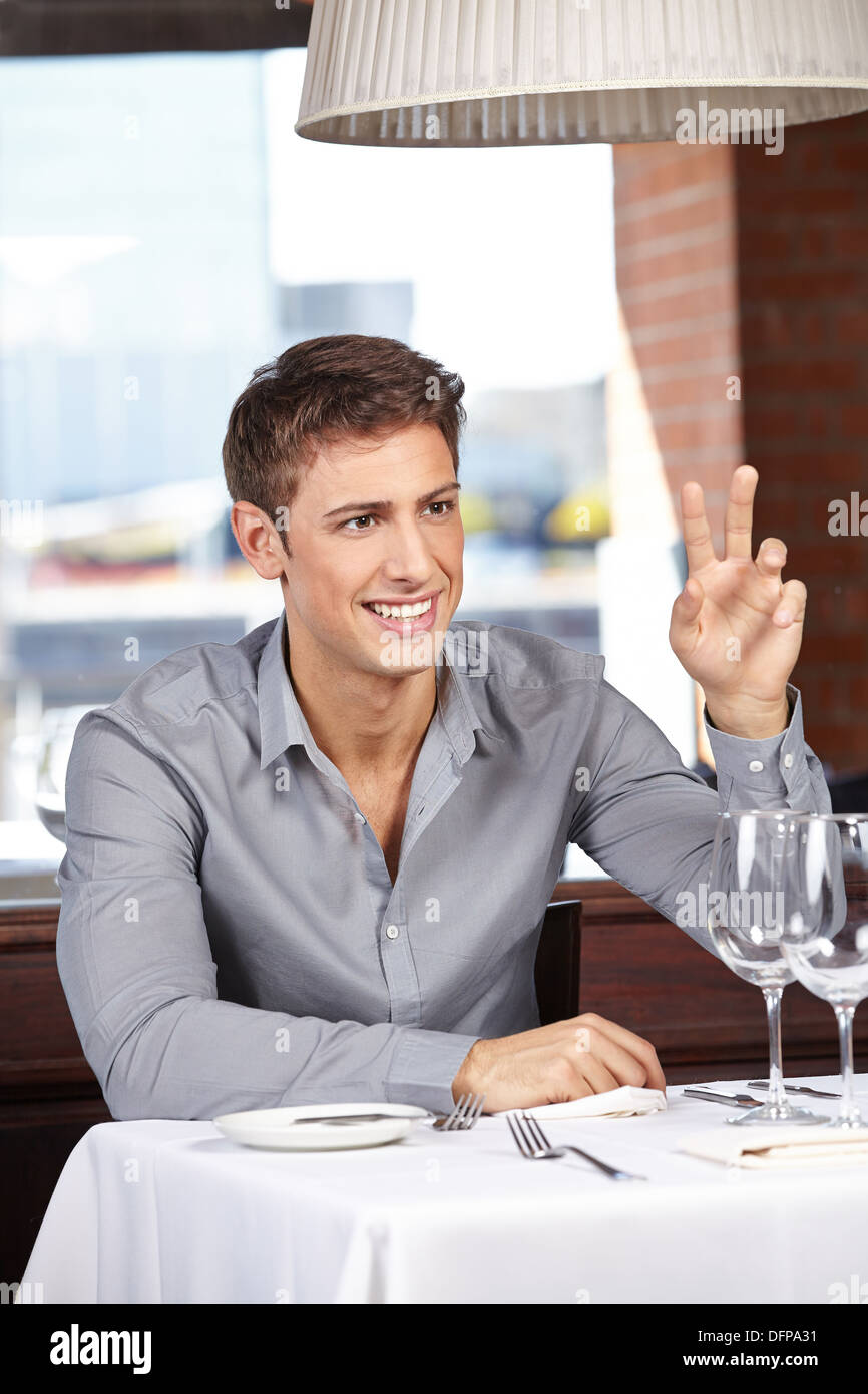 Smiling man in a restaurant calling the waiter with a hand sign Stock Photo
