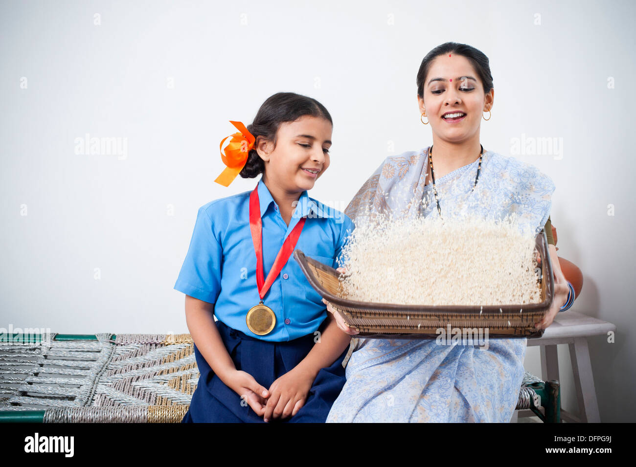 Girl sitting beside her mother winnowing rice in a basket Stock Photo