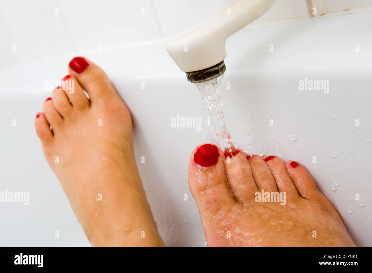 A woman is keeping her foot under the hot water of a bath faucet Stock Photo