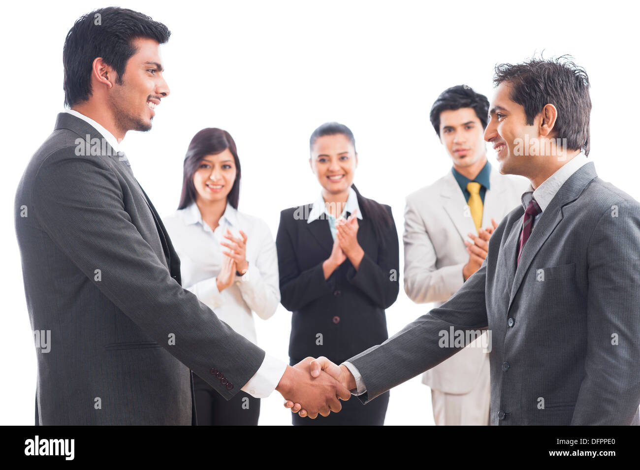 Two businessmen shaking hands with their colleagues applauding Stock Photo