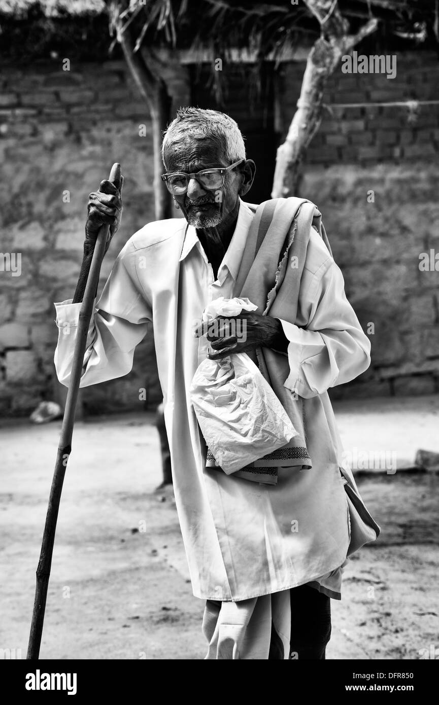 Old Indian man with walking stick going to Sri Sathya Sai Baba mobile outreach hospital. Andhra Pradesh, India. Monochrome Stock Photo