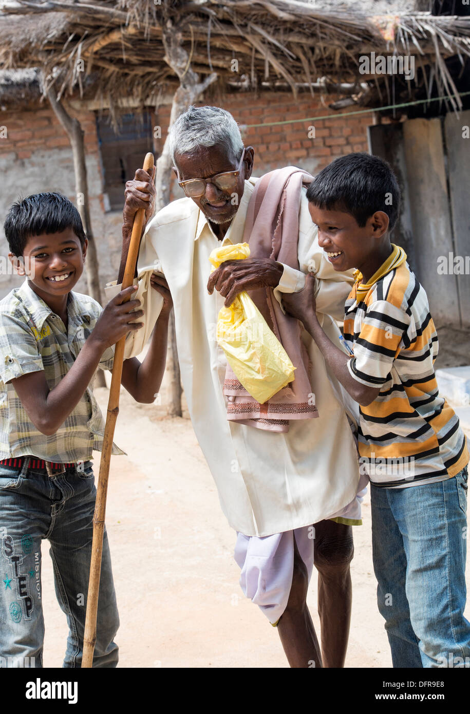 Two Indian boys helping an old Indian man with walking stick at Sri Sathya Sai Baba mobile outreach hospital. India Stock Photo