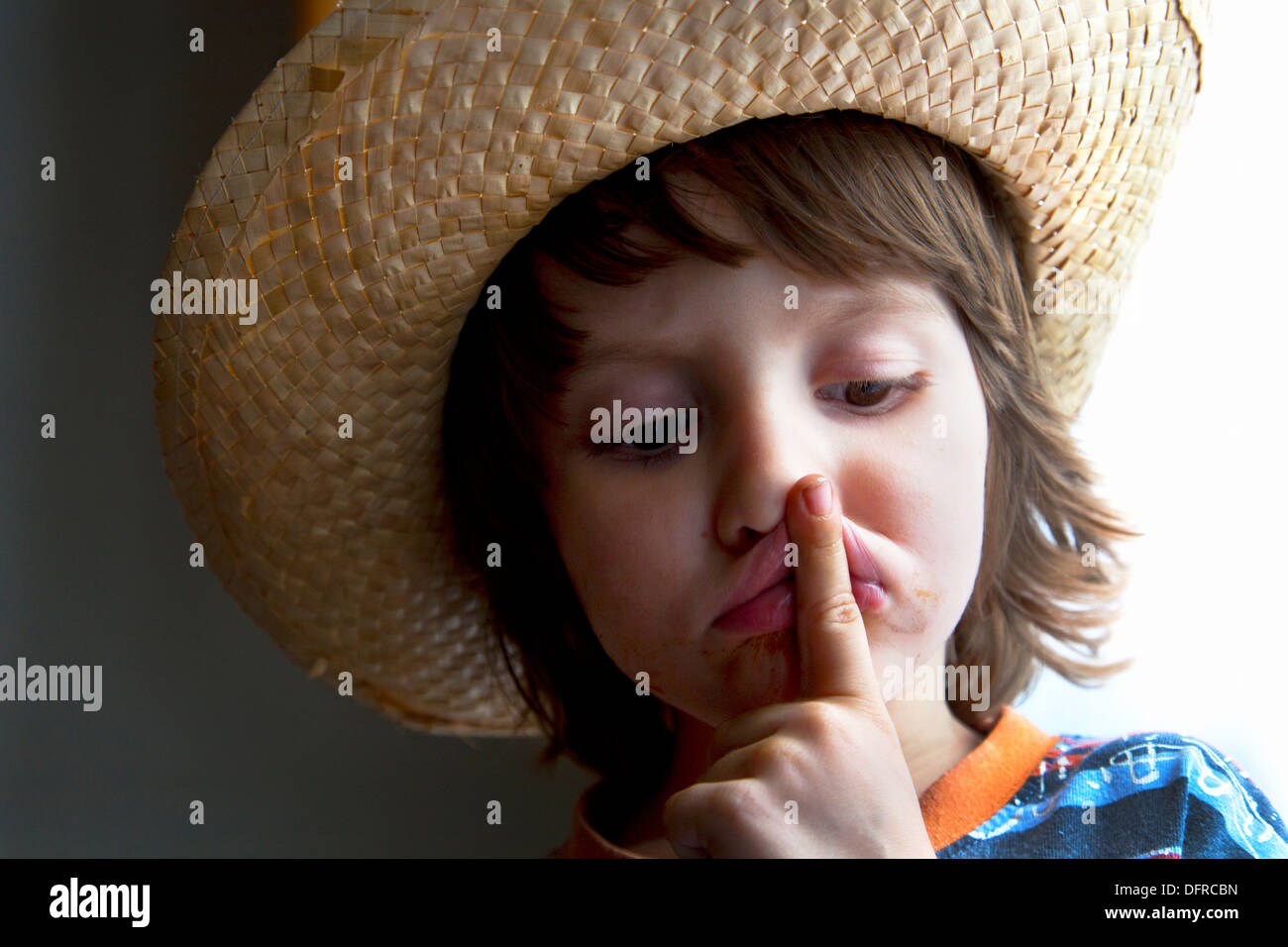 Four and a half year old boy wearing a wicker hat holding his index finger to his mouth. Stock Photo