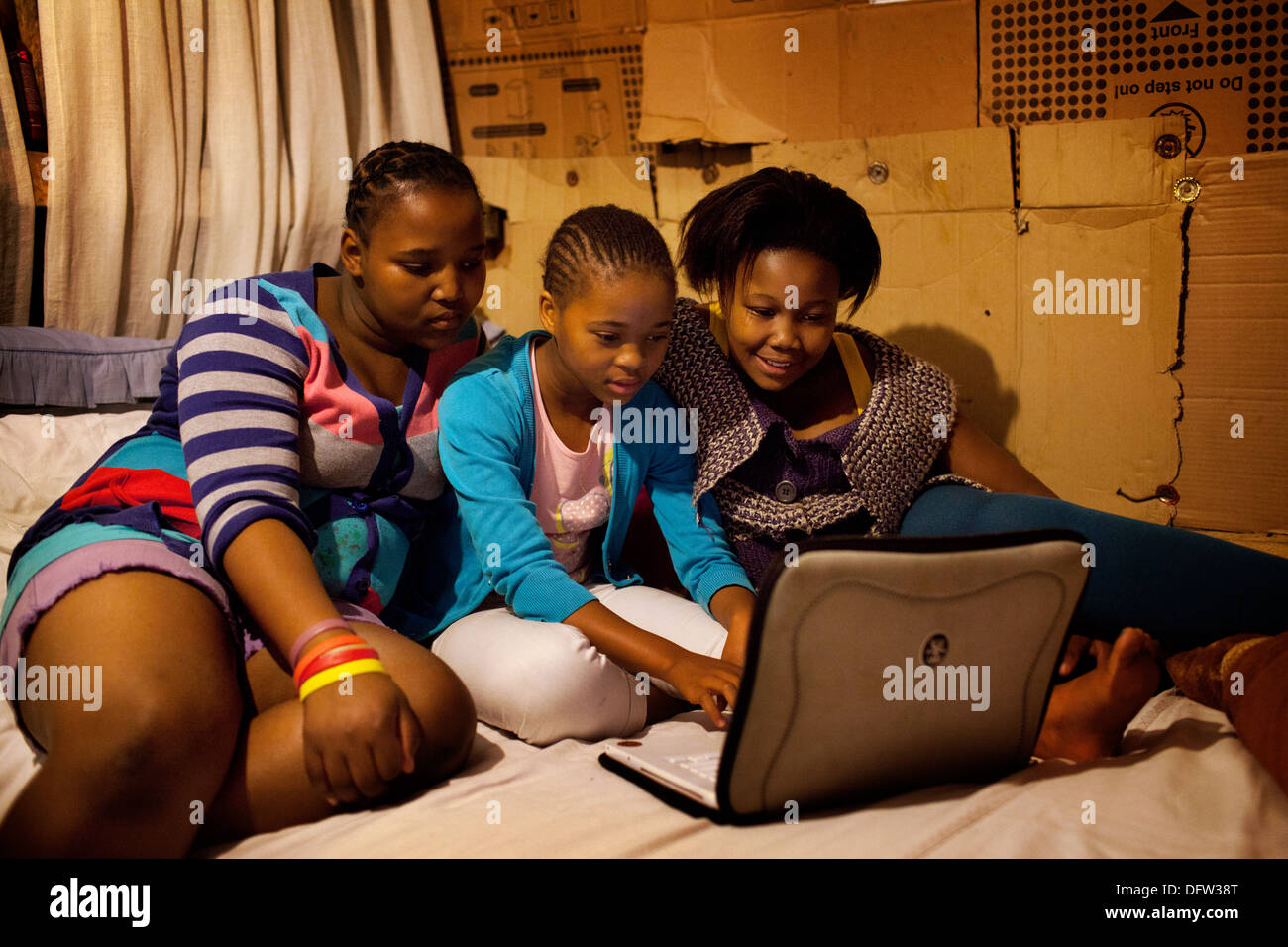 Phelela and friends doing homework on a laptop in her room in Nyanga, Cape Town, South Africa. Stock Photo