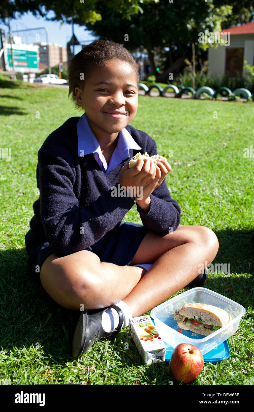 African schoolgirl eats her healthy lunch on the lawn during break at Thandokhulli school, Mowbray, Cape Town. Stock Photo