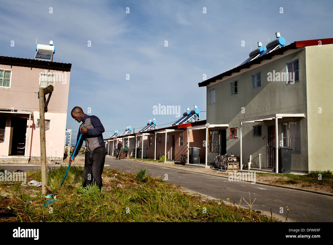 Cape Town South Africa - A man rakes a grassy patch in street a newly developed RDP housing project in Langa where all houses Stock Photo