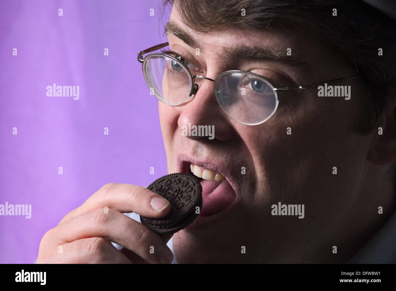 Young man, wearing glasses, eating a cookie Stock Photo Alamy