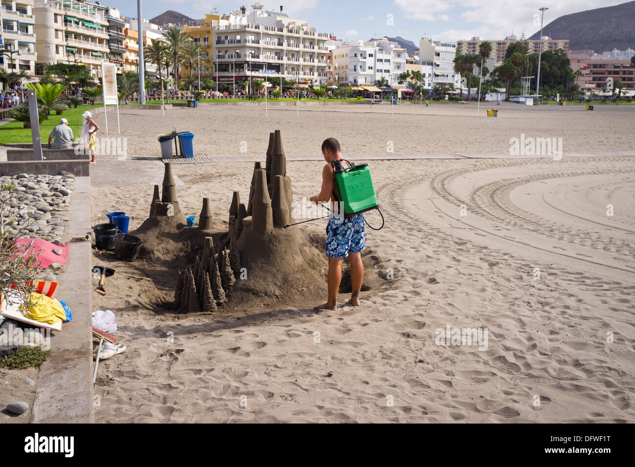 Sand sculptor sprays water from a backpack on the sand castle to preserve it, Los Cristianos beach, Tenerife, Canary Islands, Stock Photo