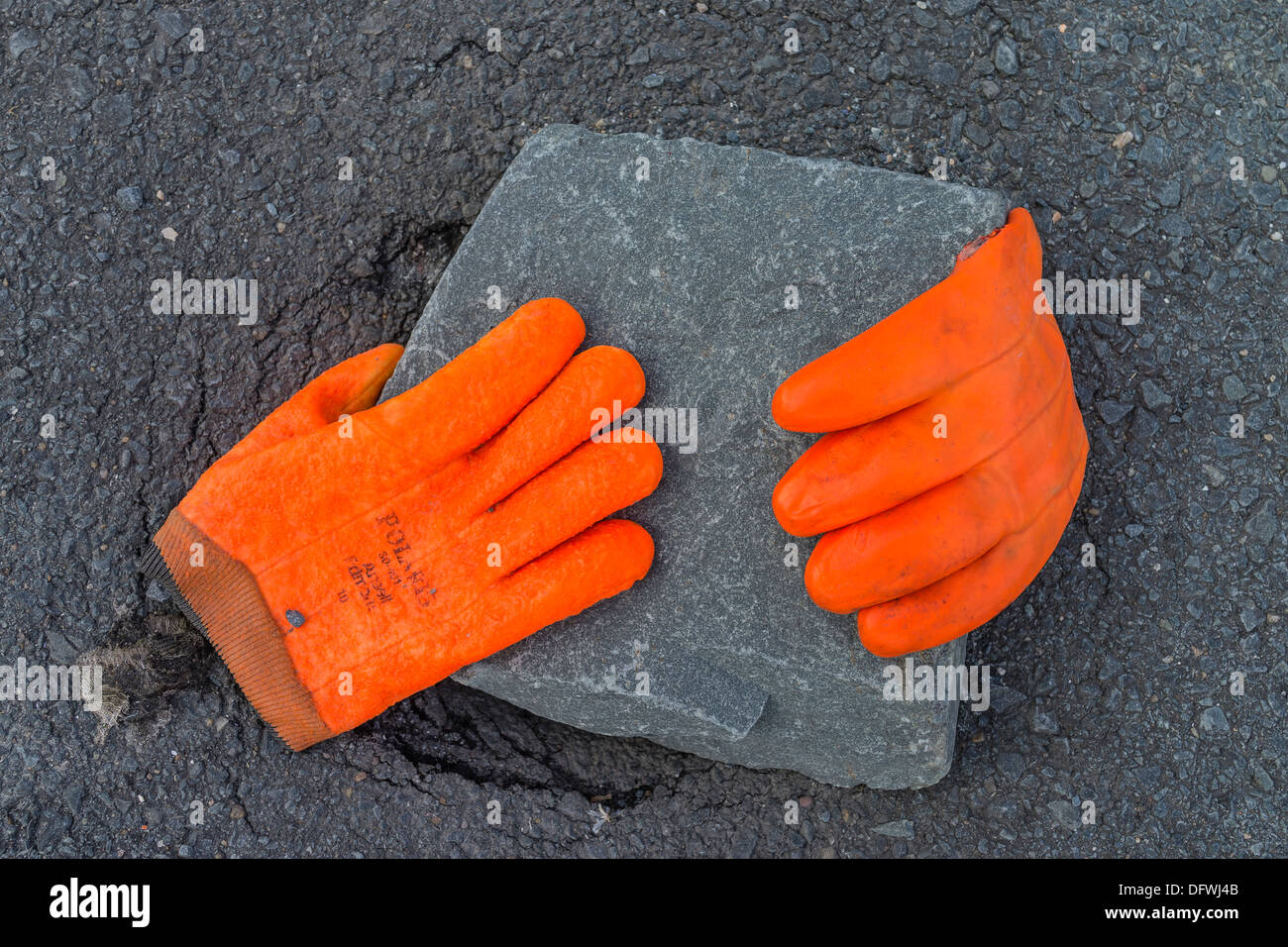 A pair of bright fluorescent orange worker's gloves lay over a gray stone paver on the street in Peggys Cove, Nova Scotia. Stock Photo