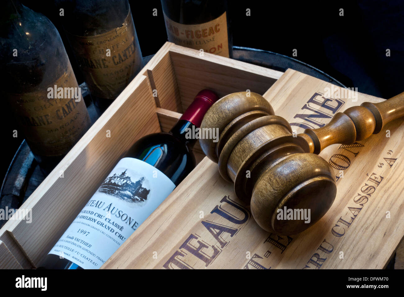 Wine auction cellar with gavel on open case of Chateau Ausone Saint-Émilion red wine and other old fine red Bordeaux wine bottles behind France Stock Photo