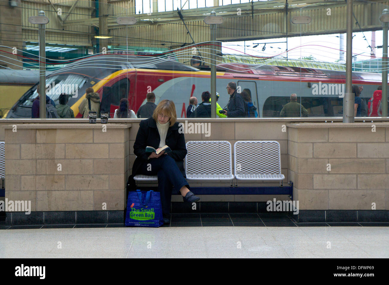 Woman passenger reading a book waiting at Carlisle Railway Station Carlisle Cumbria England United Kingdom UK Stock Photo