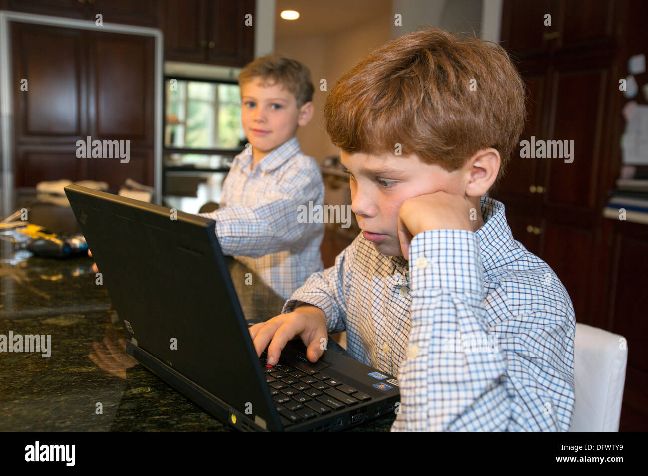 Birmingham, Michigan - Gaspard Mosquet, 11, works on a laptop computer while his brother Artus, 8, watches. Stock Photo