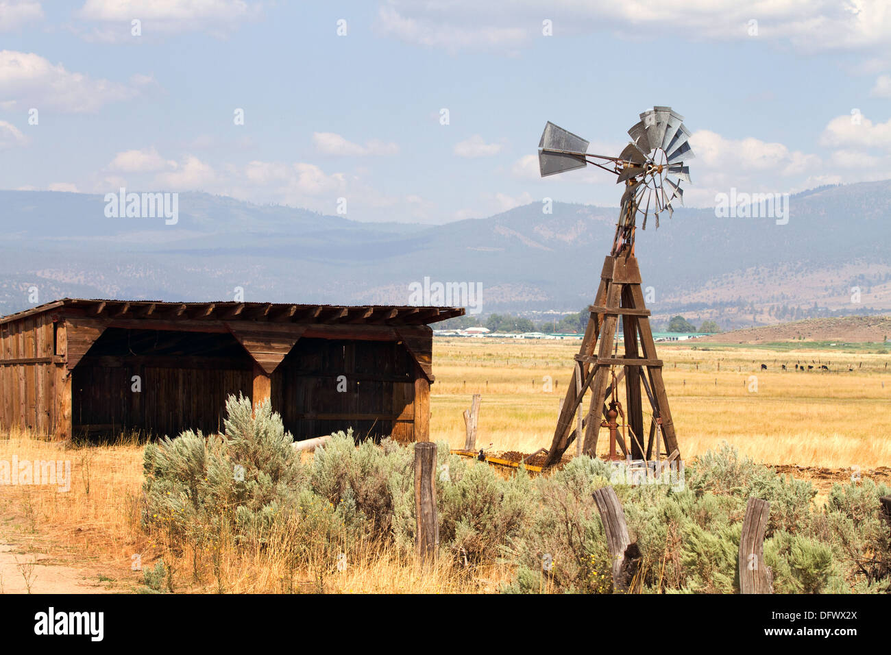 Old wind driven water pumping windmill stands next to an empty storage shed on a cattle ranch in a California mountain valley. Stock Photo